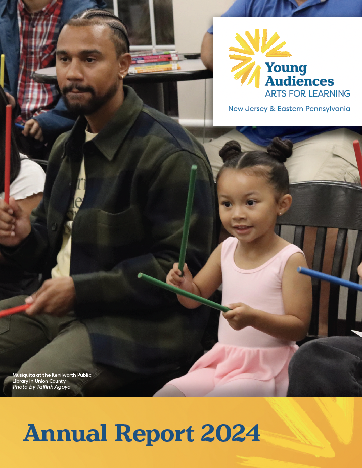 Father sitting next to little girl in a ballerina outfit hitting drum sticks together.